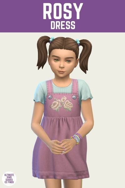 This is a product image for an item from The Playground Set by Joliebean. This image has a purple bar at the top with white text that says "Rosy Dress" and there is a girl child posing. They have pig tails and are wearing a pink overall dress over a teal t-shirt 