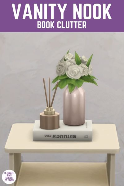This image has a purple bar at the top with white text that says "Vanity Nook Book Clutter" below that is a table with a book on its side and on top is a flower vase and beside that is a stick diffuser. 